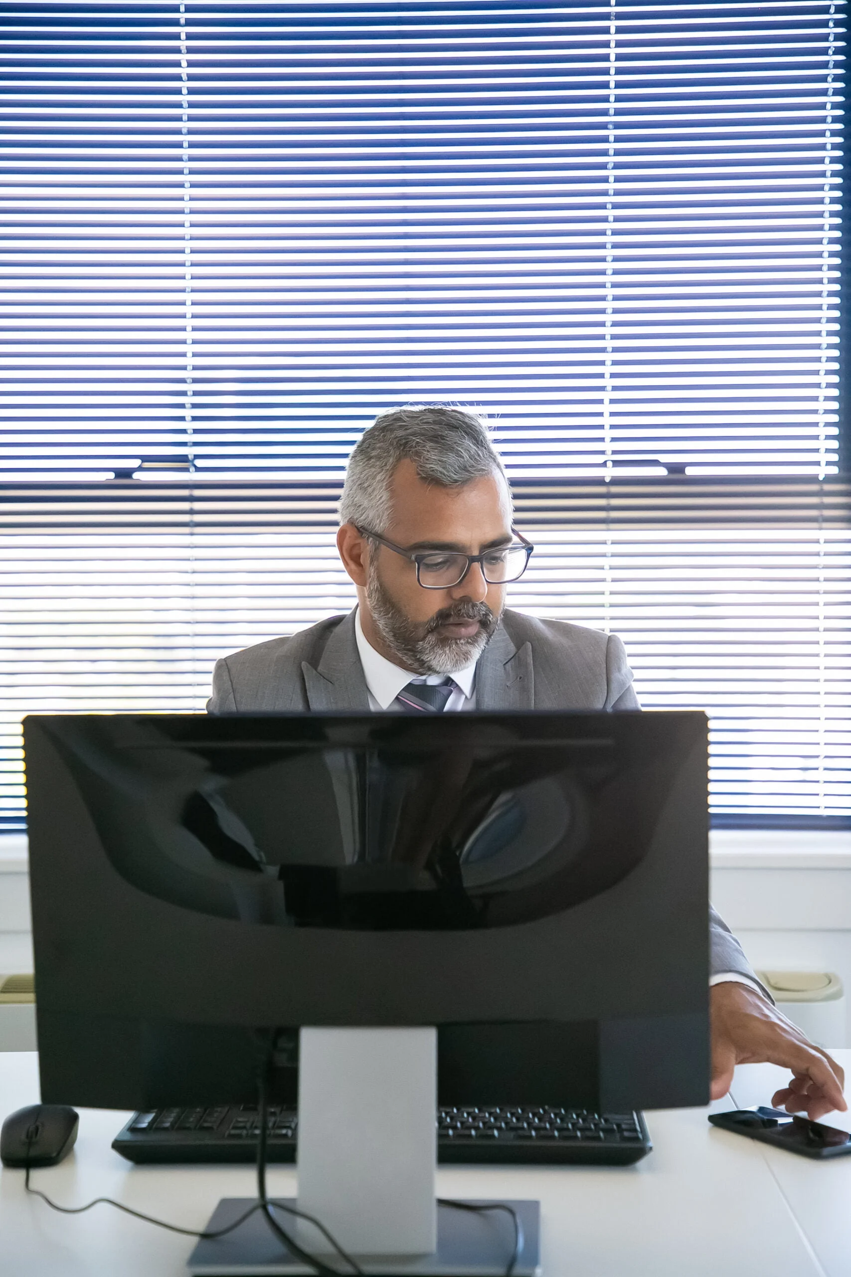 Serious grey haired businessman sitting at workplace
